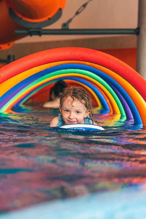 Kind schwimmt im Hallenbad des Hotels Babymio durch bunte Schwimmreifen