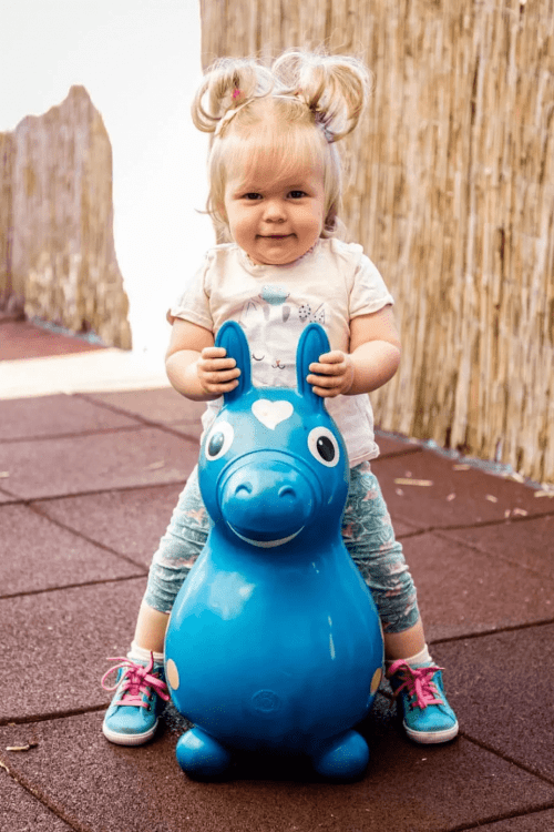 Kleinkind spielt auf einem blauen Hüpfpferd